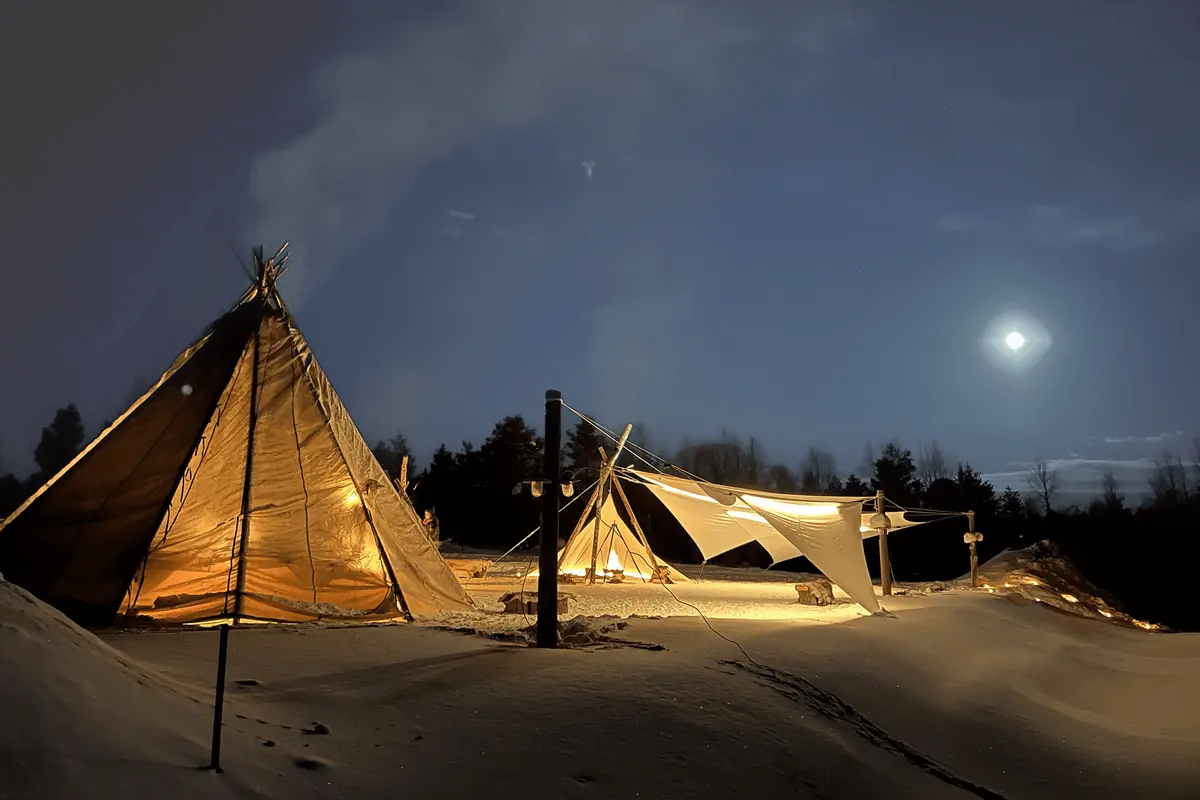 A warmly lit lavvu and open-sided stretch tent on moonlit snow at a Michelin influencer event in Finnish Lapland